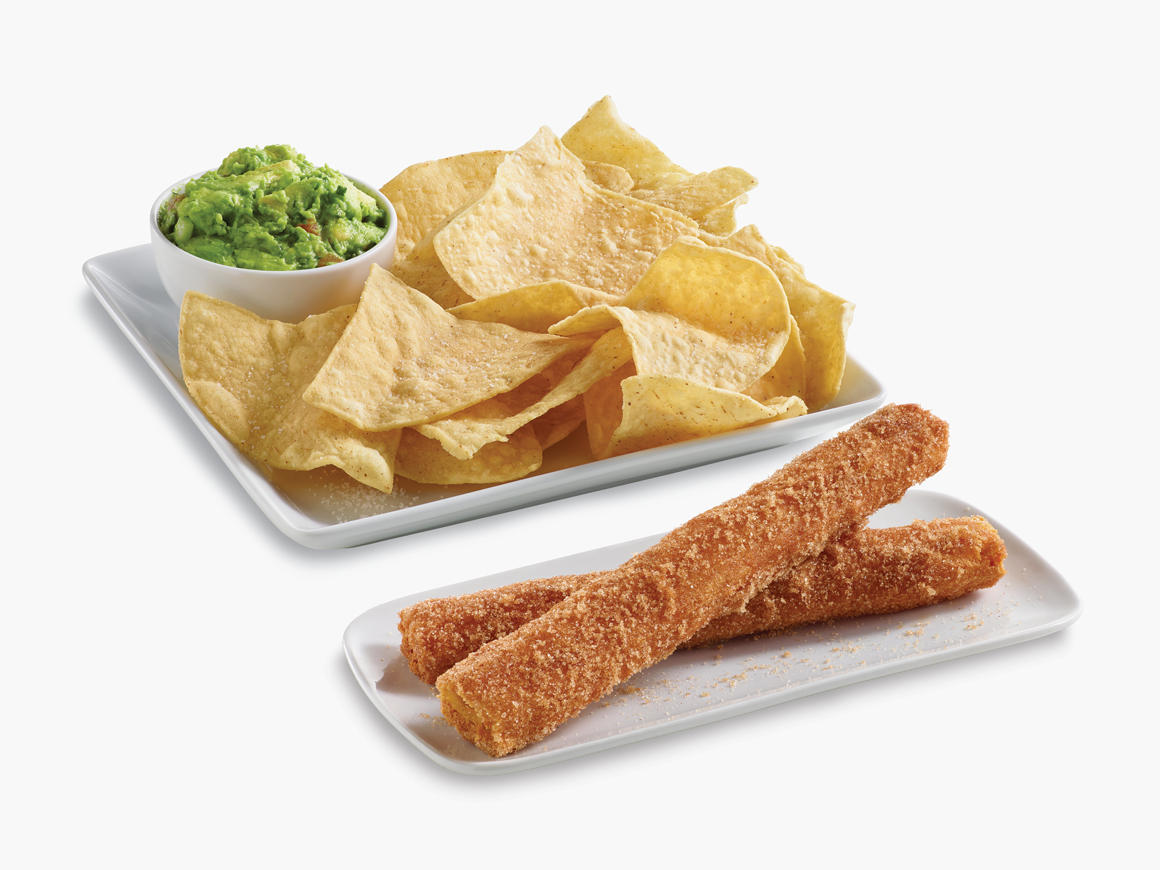 Chips and a side of guac on a black plate.